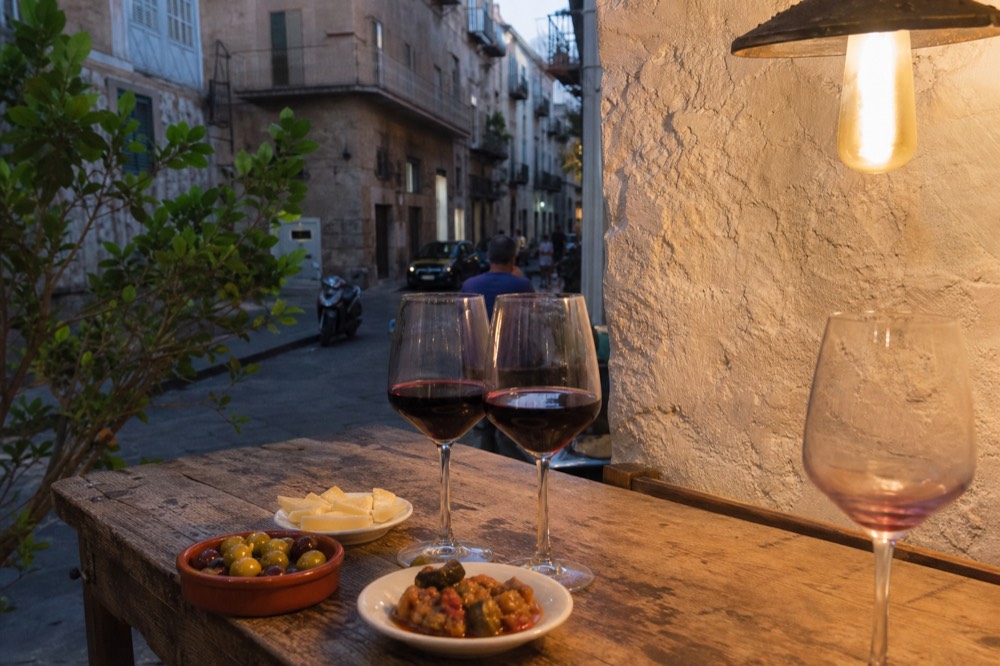 Glasses of red wine and small plates of Sicilian tapas on a wooden counter