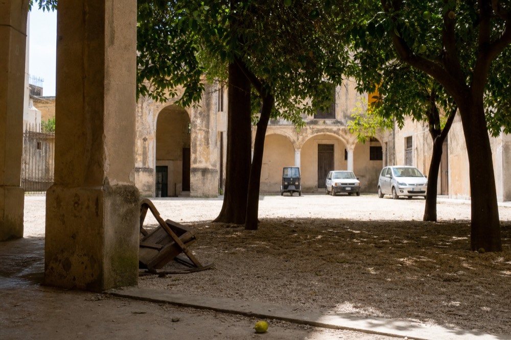 An empty sunlit courtyard with orange trees and stone arches