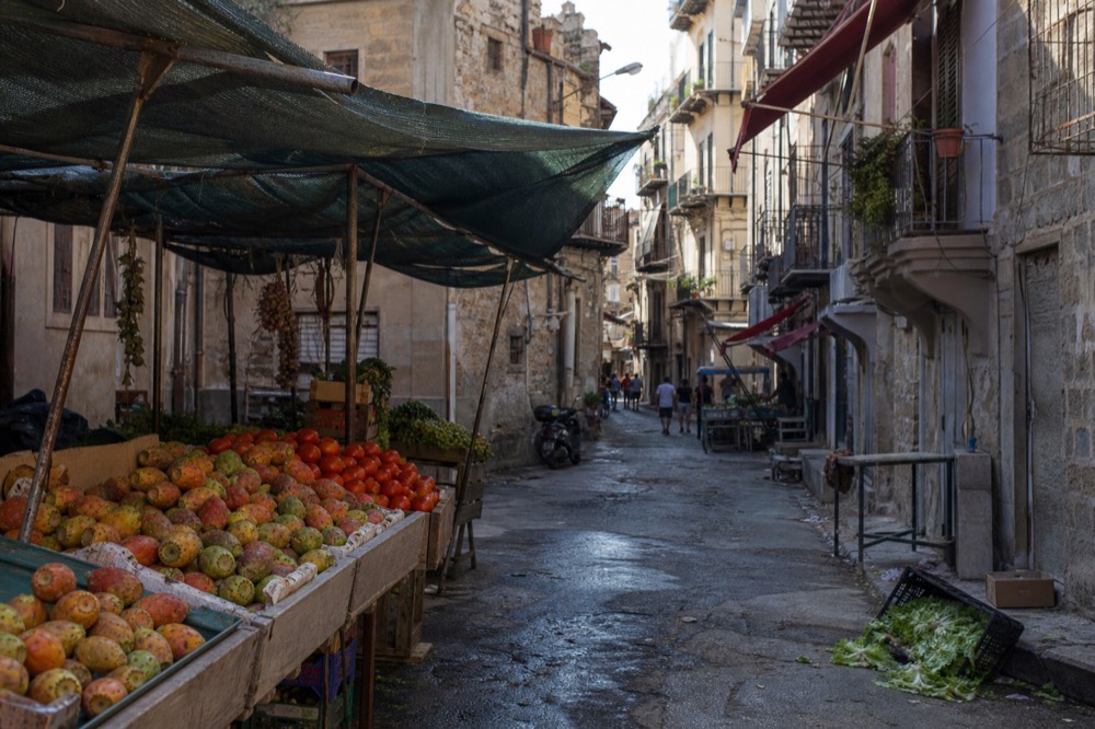A narrow Palermo market street lined with produce stalls under canvas awnings