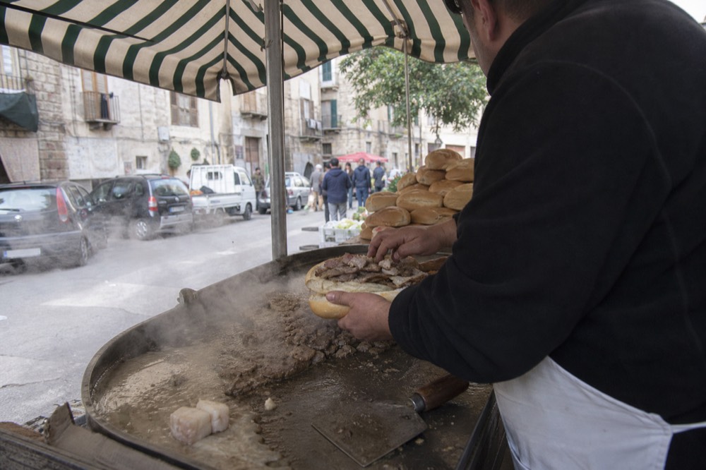 A street vendor in Palermo assembling a pane ca meusa sandwich with a cleaver