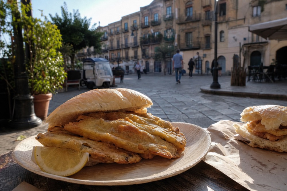 A close-up of a panelle sandwich with chickpea fritters and lemon on a wooden plate