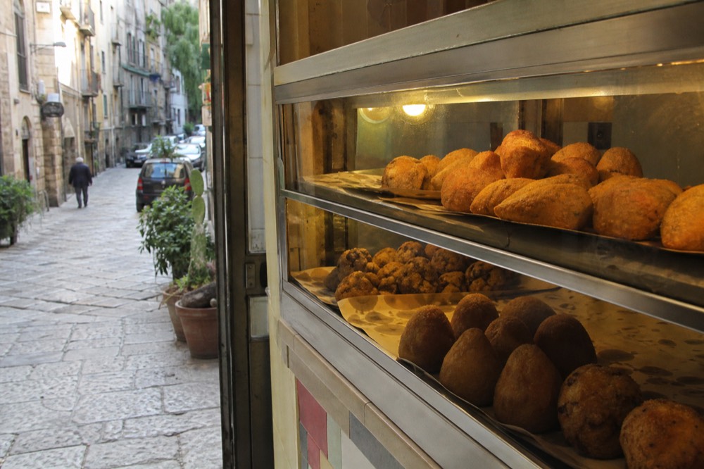 Golden fried arancine and chickpea fritters in the display case of a Palermo food shop