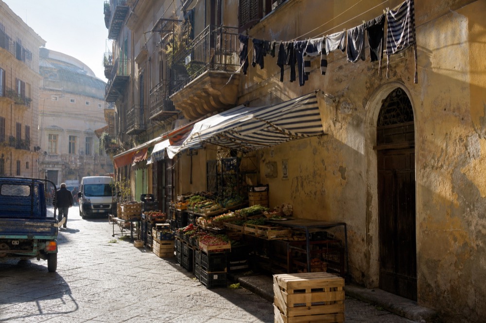Market stalls with fresh produce under awnings in a Palermo street