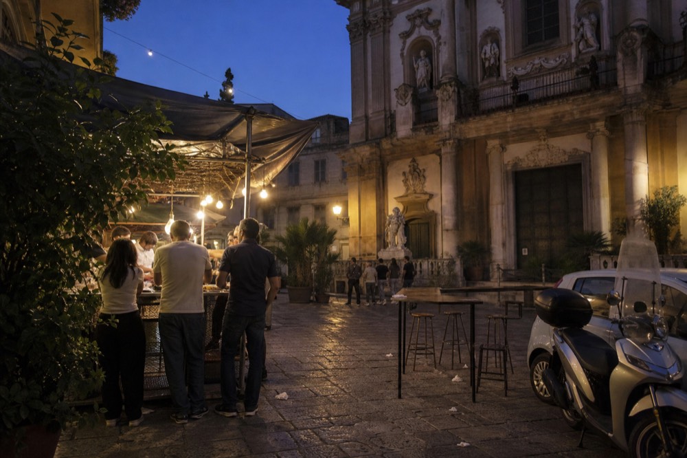 An evening food stall glowing under lights in a Palermo square