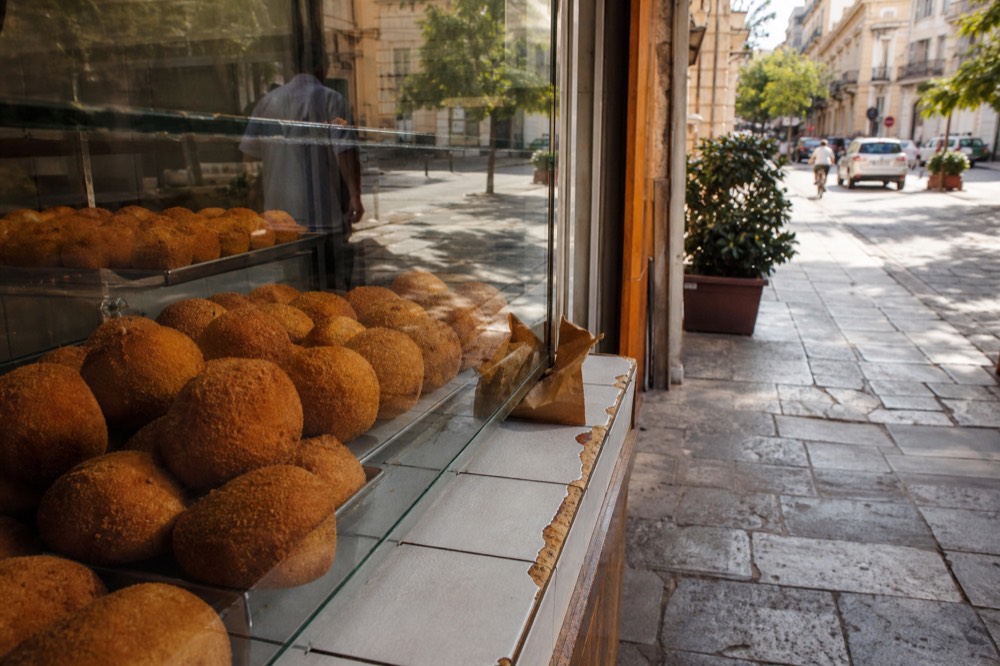 Round golden arancine arranged in a Palermo bakery display case