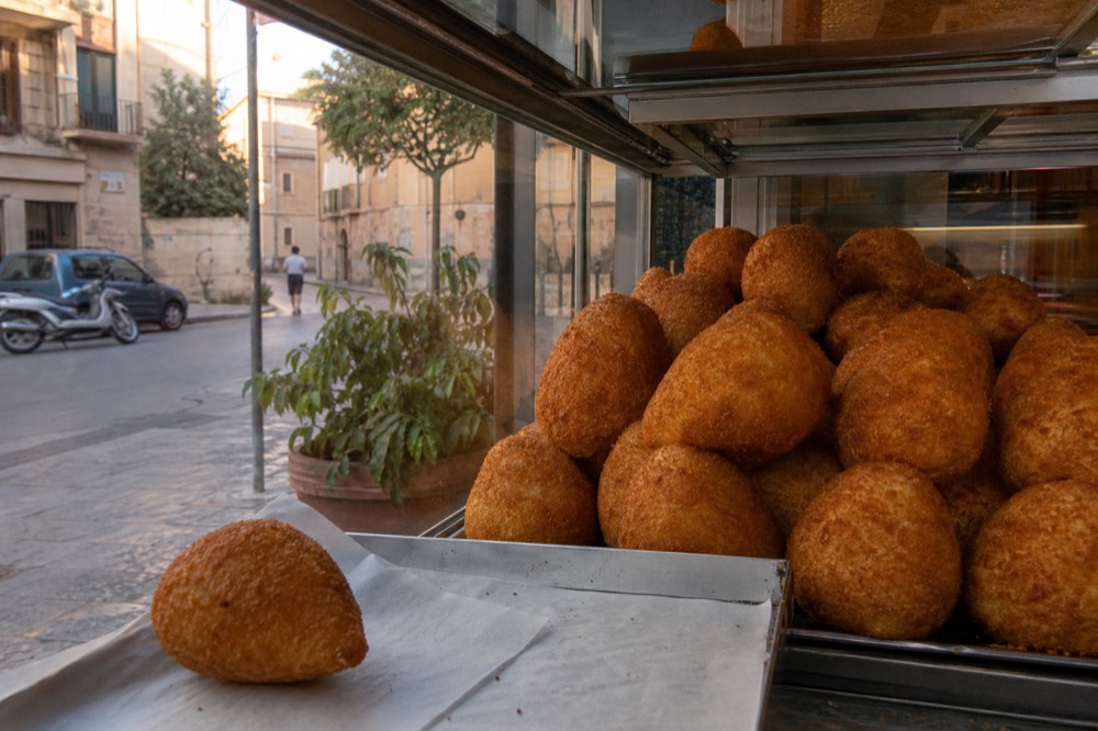 Round golden arancine stacked in a glass display case at a Palermo bakery