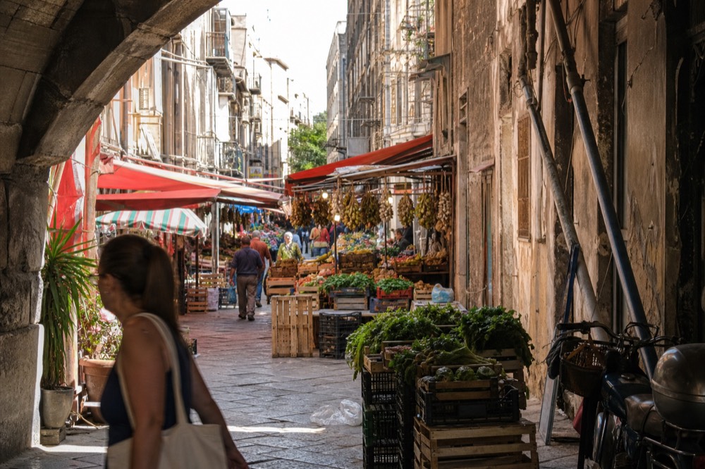 Crowded Palermo market lane with hanging produce and colorful food stalls