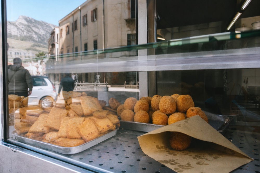 Fried panelle and arancine stacked in the glass display case of a Palermo street food shop