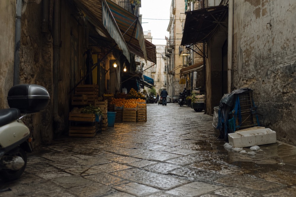 Narrow Ballaro market lane with striped awnings, stacked crates and hanging shop signs