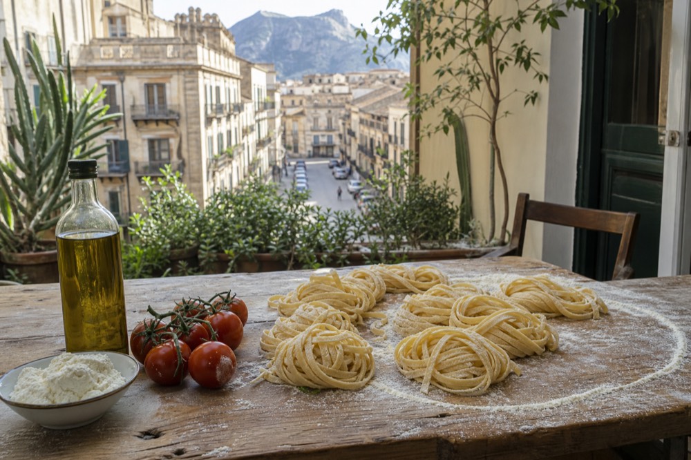 Fresh pasta, flour and Sicilian ingredients laid out on a wooden kitchen table