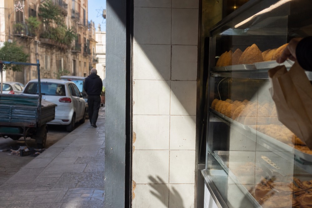 Golden rice balls and fried snacks displayed in a Sicilian bakery window