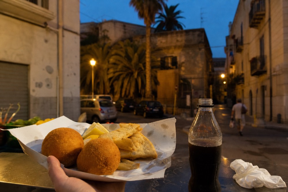 Fried arancini and panelle served on a paper tray at a market stall