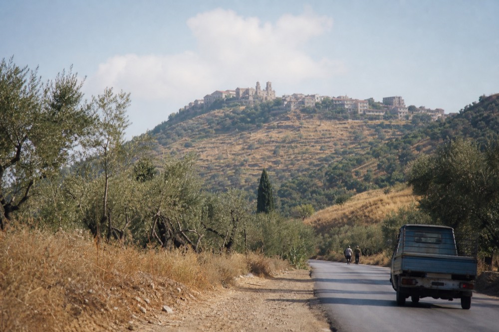 Olive groves and hills on a Sicilian countryside road toward a distant hilltop town