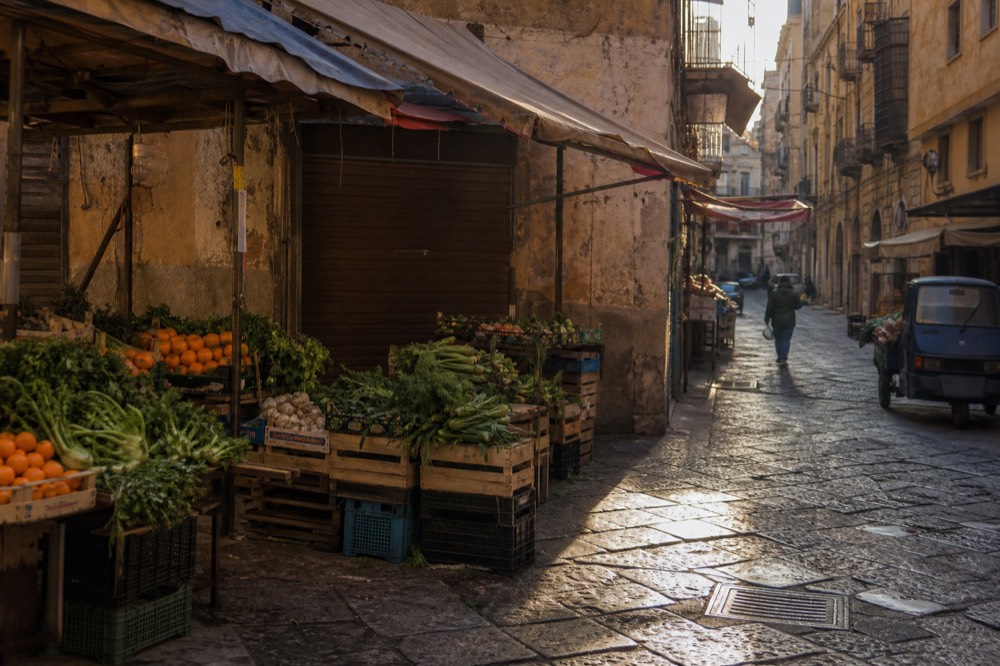 A Palermo market street with produce stalls and canvas awnings in the morning