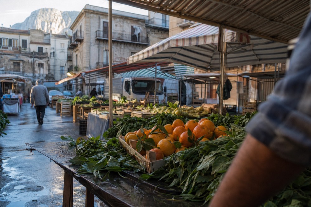 Market stalls with crates of oranges and leafy vegetables under striped awnings