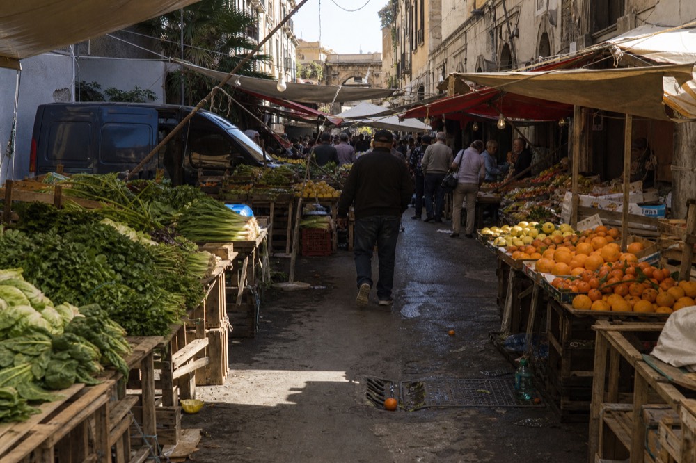 Crowded market lane with produce displays and awnings in full daylight