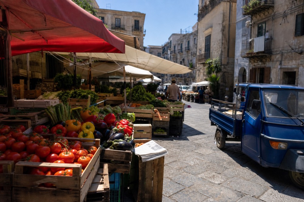 Market awnings and produce stalls in bright sunshine on a Palermo street