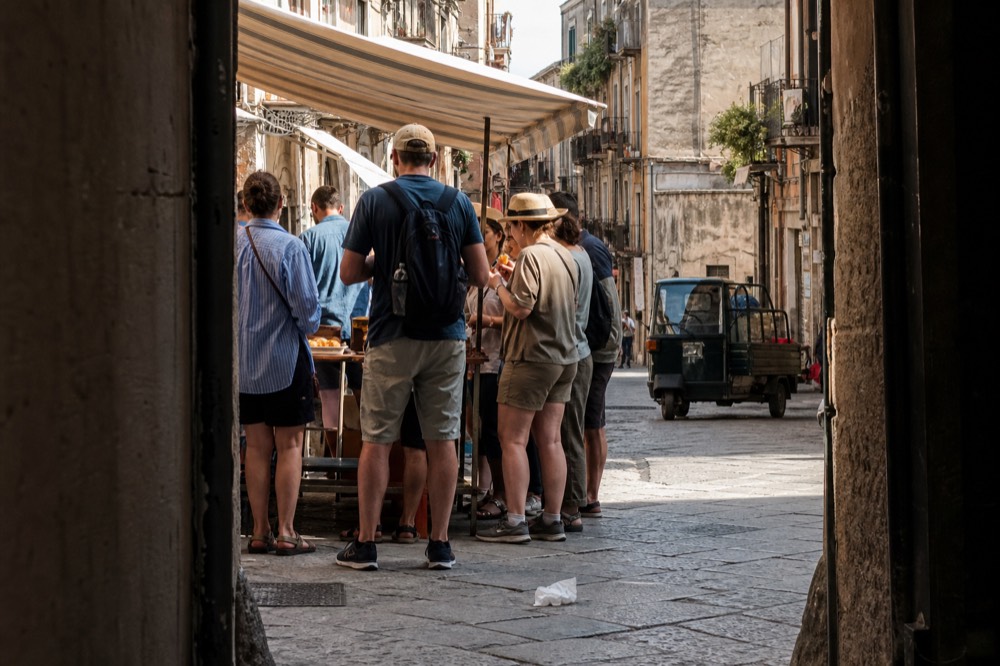 A food tour group sampling arancine at a Palermo market stall