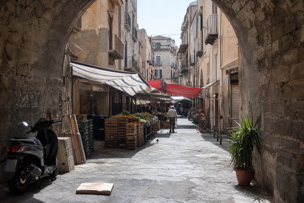 A market alley in Palermo with produce crates, striped awnings and shop signs above the stalls