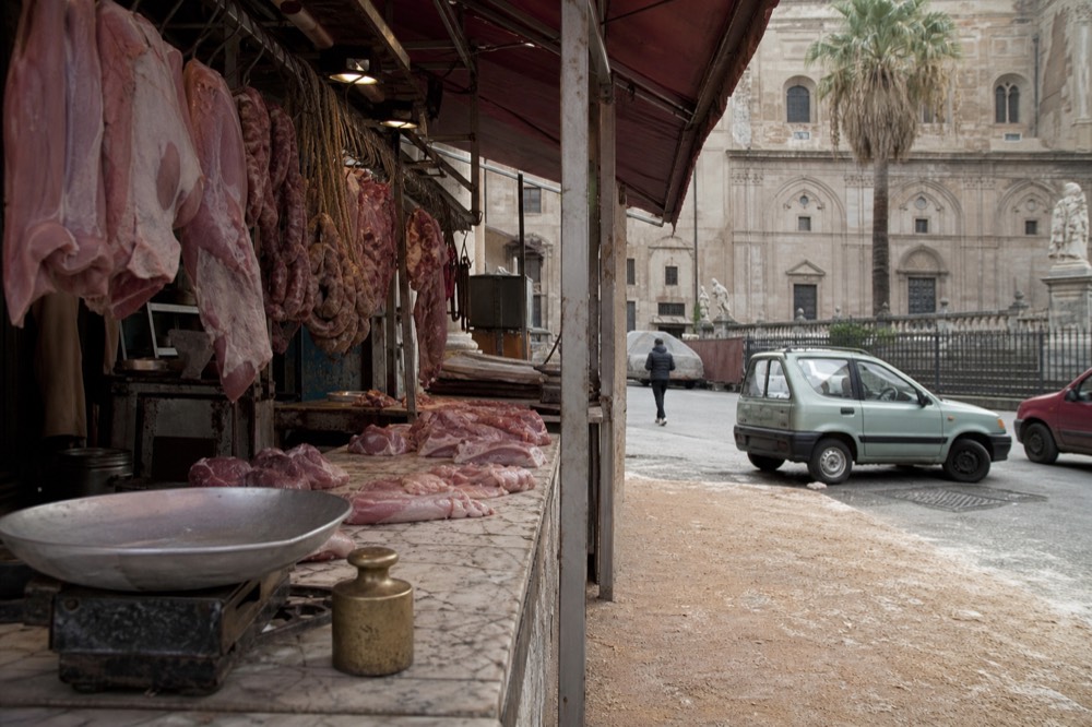 A butcher's stall in a Palermo market with hanging meat and a marble counter