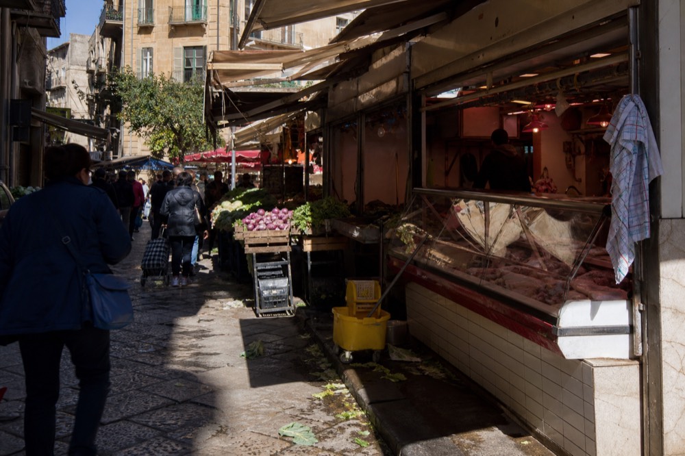 A busy Palermo street in morning light with pedestrians walking between market stalls