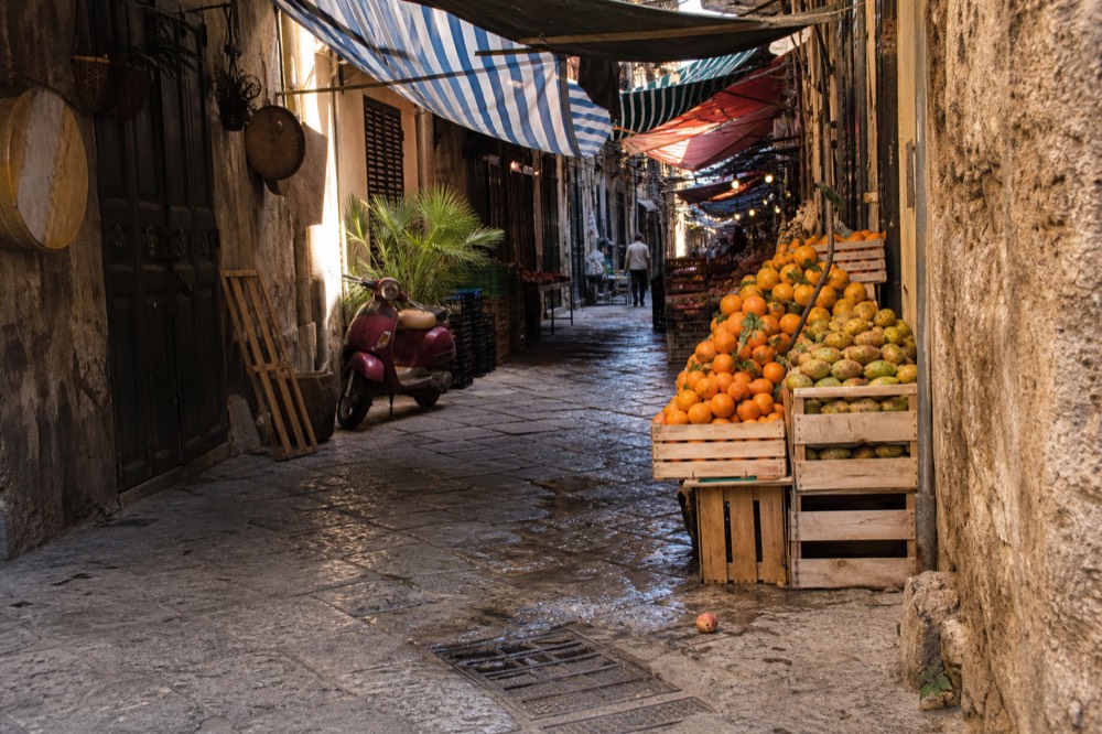 A narrow Palermo market street lined with colorful awnings and stacked fruit crates