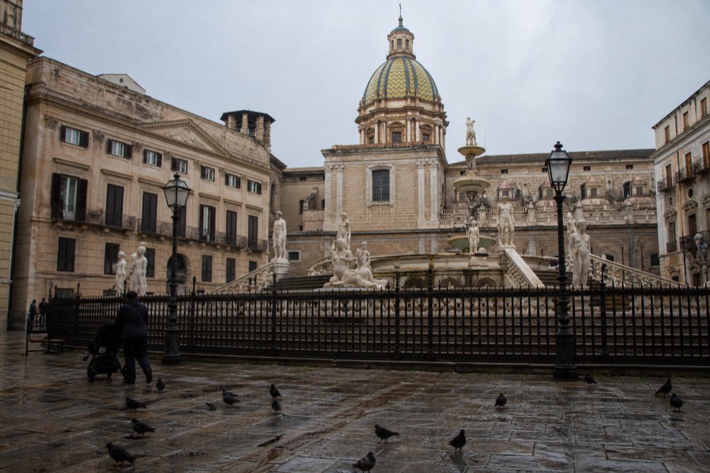 A baroque square with a fountain and ornate building facades in Palermo