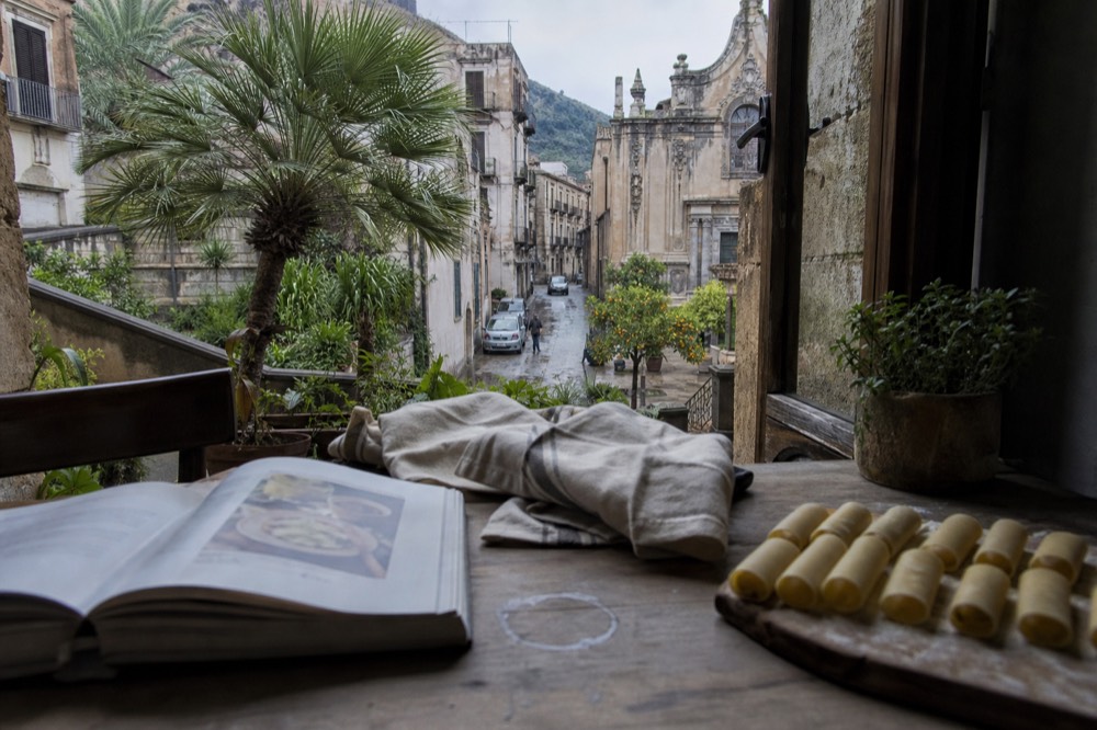A wooden table with a recipe book, apron and rolled fresh pasta tubes