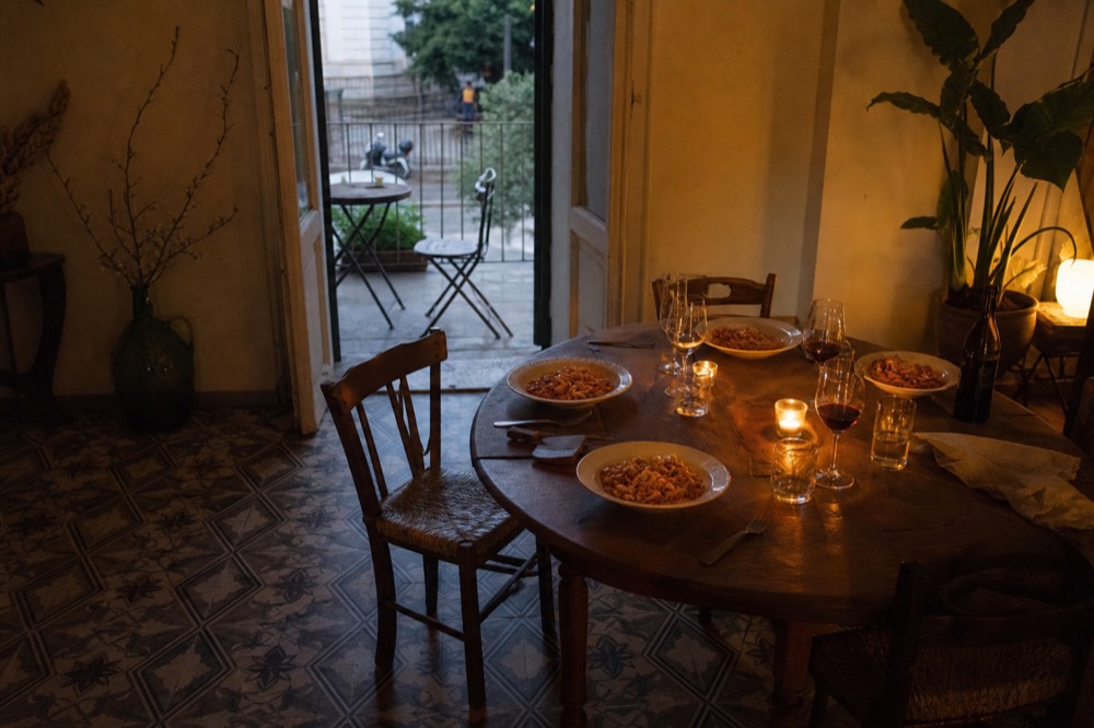 A dining table at dusk with candles, wine and plates of pasta ready to serve