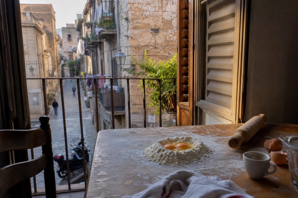 A kitchen table with flour, eggs, a rolling pin and fresh pasta dough