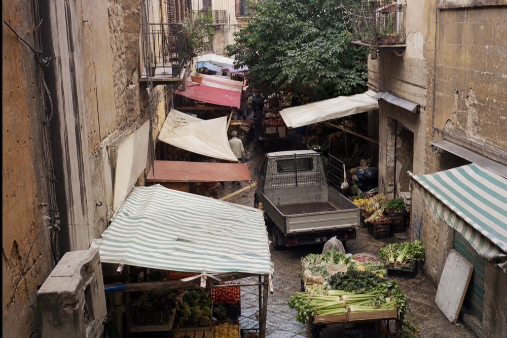 Stalls with colourful produce lining a narrow Palermo street