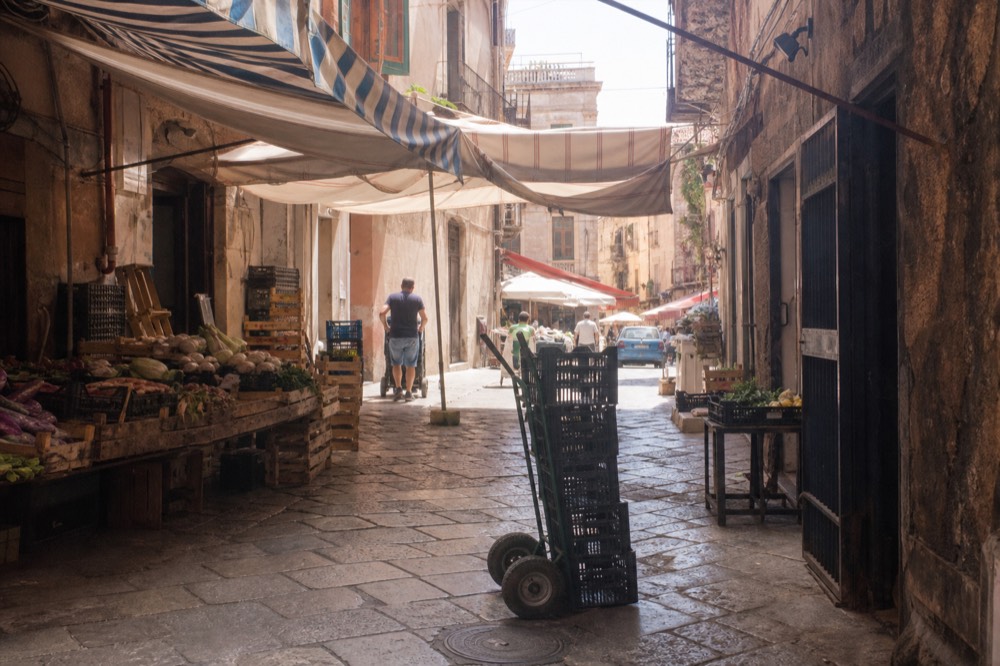 A narrow Palermo market street with striped awnings and produce stalls