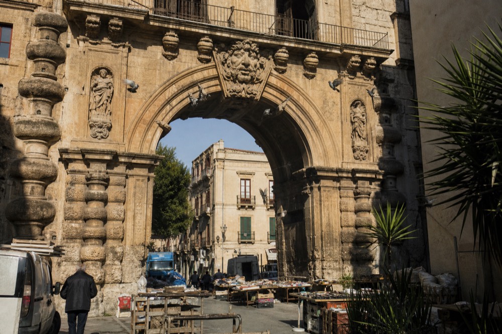 A historic stone gate archway over a market street in Palermo