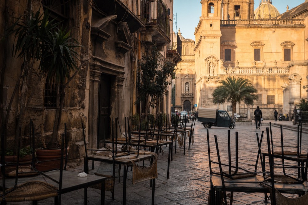 Golden late afternoon light on a Palermo square with empty bar tables