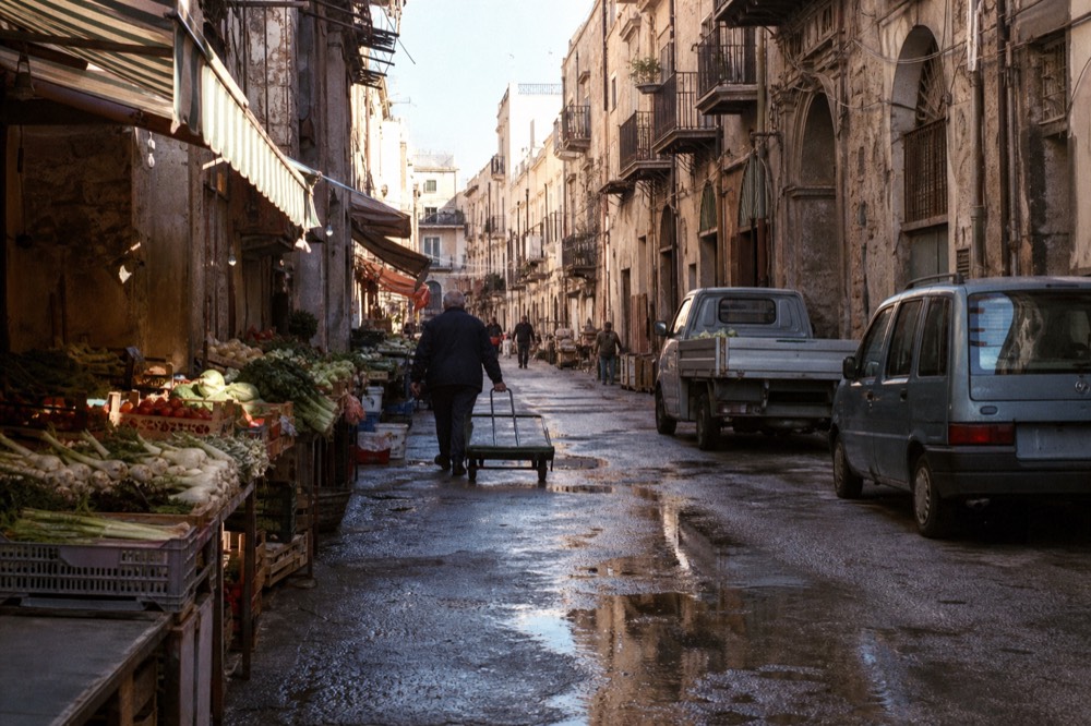A Palermo street food vendor slicing sfincione on a crowded market alley