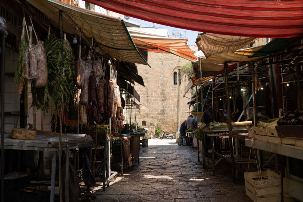 A covered market lane with hanging produce and striped awnings