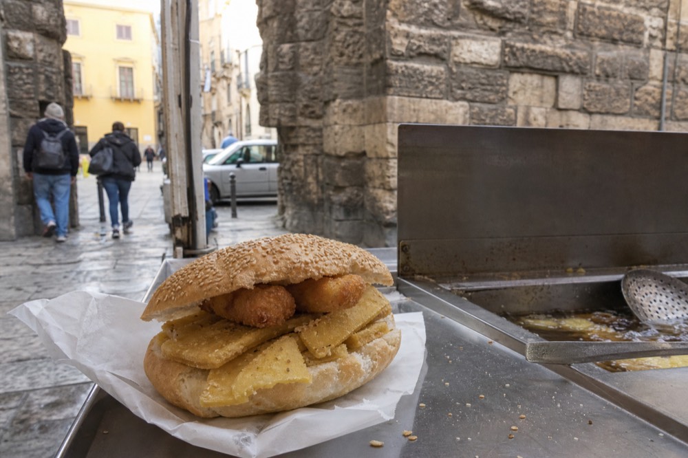 Fried chickpea fritters and potato croquettes served in a sesame roll at a market counter
