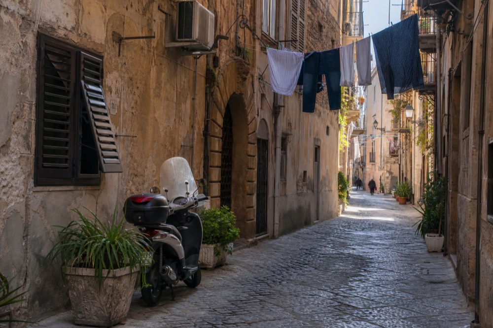 A quiet Palermo side street with worn facades and hanging laundry in morning light