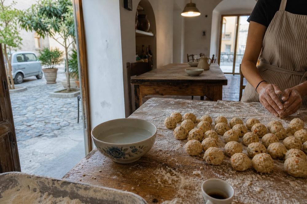 Hands shaping rice balls for frying on a floured wooden kitchen table
