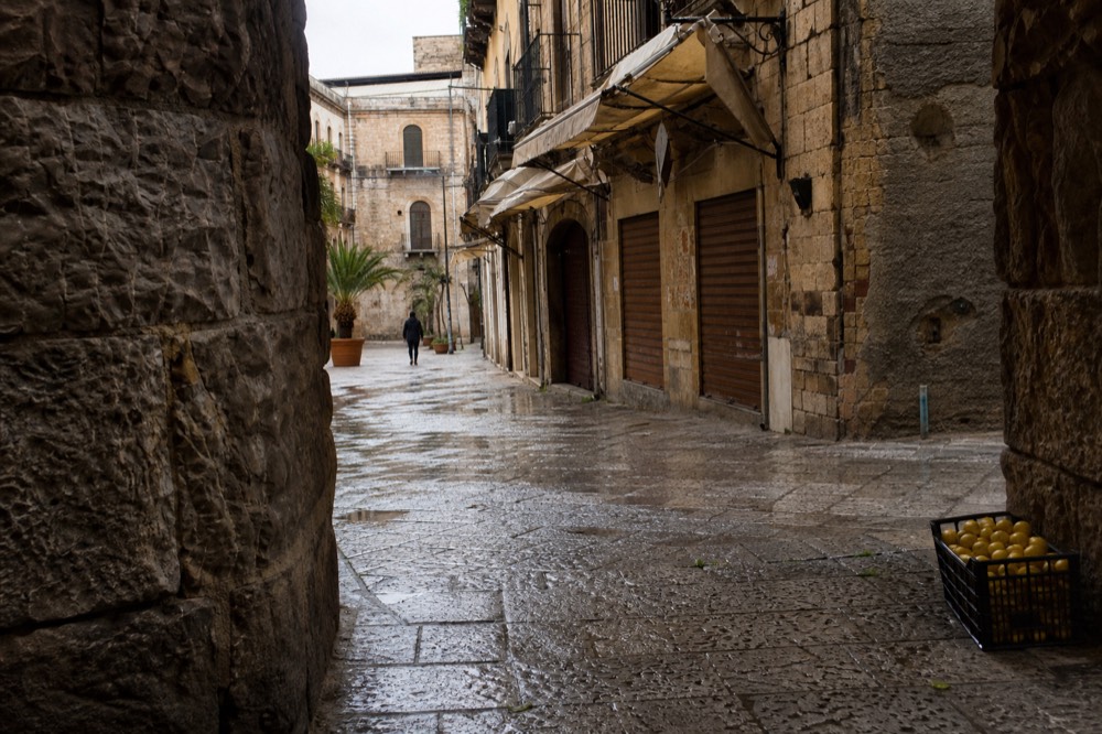 Porticoed square with closed shutters and scattered market awnings in morning light