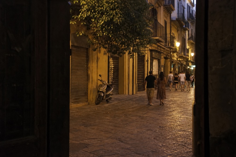 A pedestrianised Palermo street in the evening with people walking past closed food shops