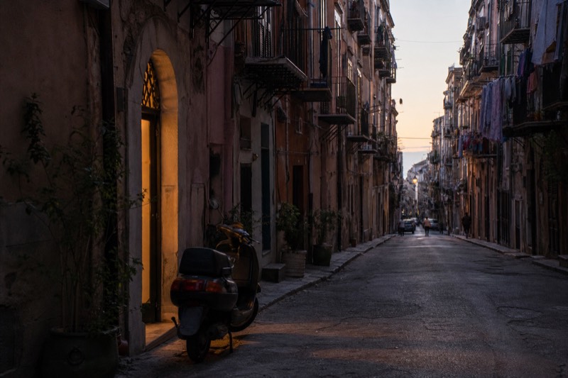Iron balconies on a tall old-town street in central Palermo at dusk.