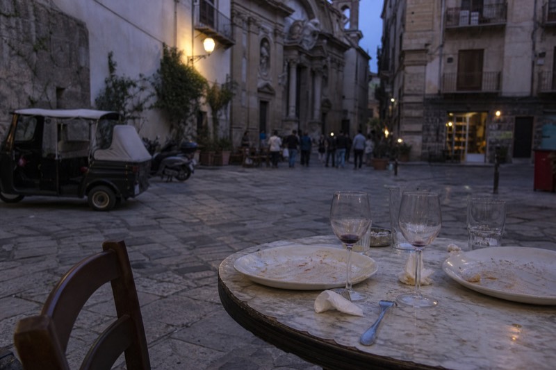 A shared table after a meal in Palermo, empty plates and glasses left behind.