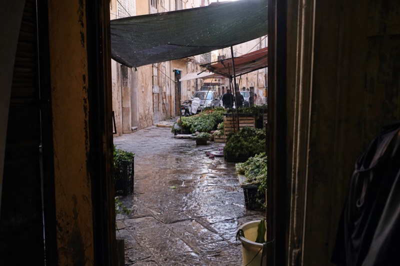A narrow Palermo lane crowded with market stalls under strung awnings.